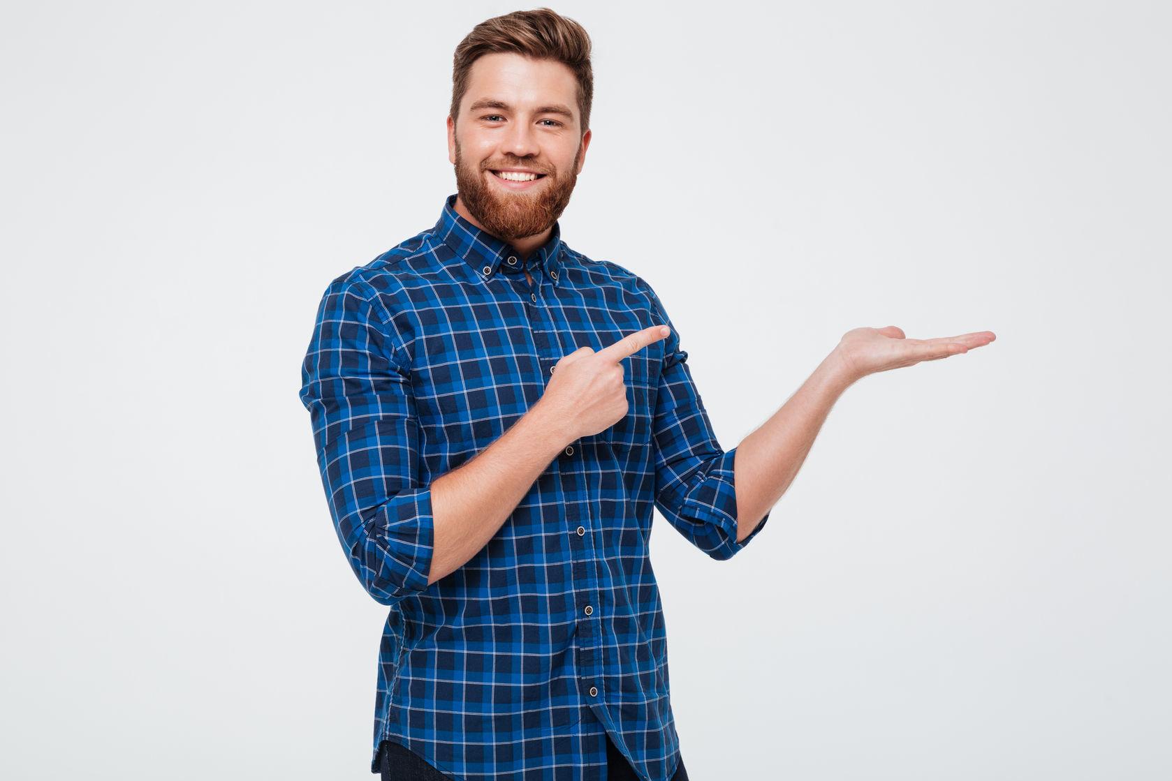 Excited smiling bearded man pointing finger at copy space on his palm isolated over white background